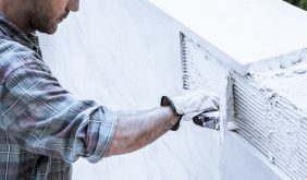 A worker applies cement to a wall with a scraper to fix the tiles.