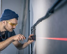An electrician is mounting electric sockets on the white wall indoors.