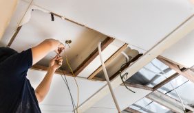 Electrician concealing electicity power wire lines within plastic tube embeded into ceiling